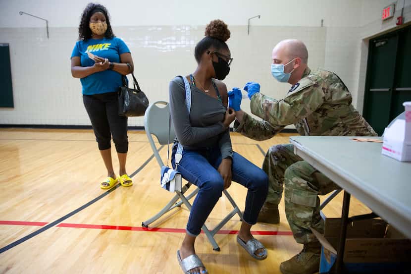 Nijah Cook (CQ), 16, receives the Covid vaccine from Spc. Derek Hurtado (right) as mother...