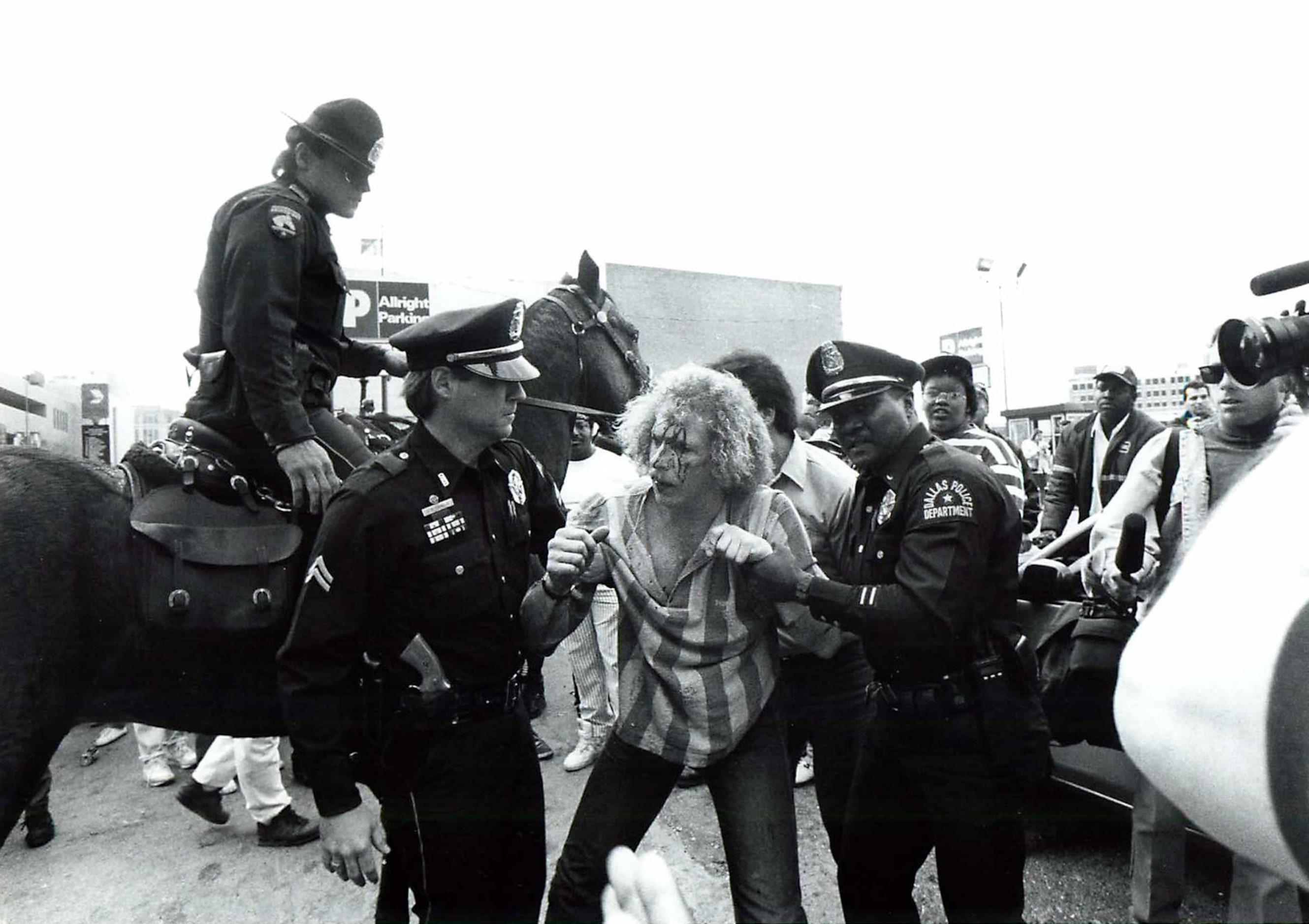  Dallas police officers lead a bloody, unidentified man to a waiting ambulance February 9,...