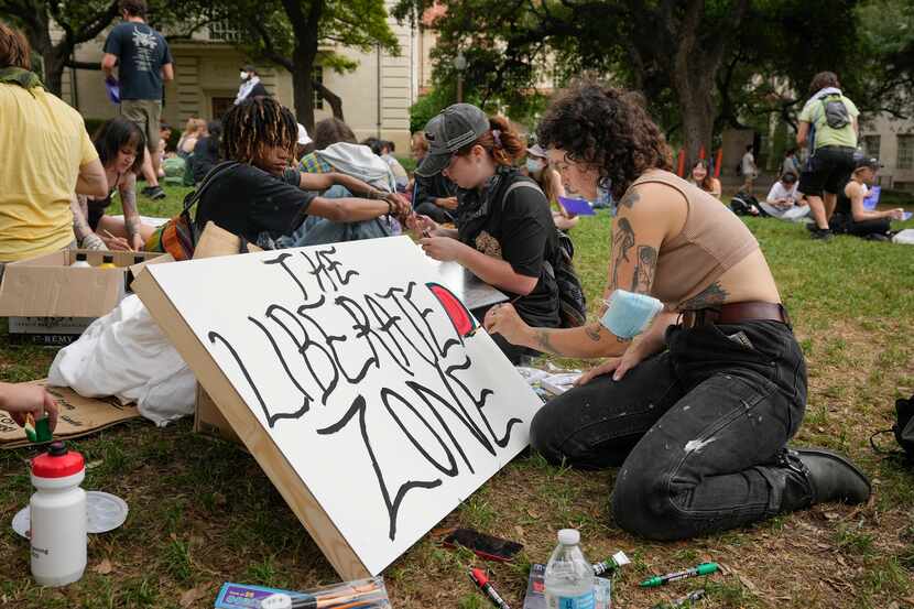 A UT Austin student paints a sign for a "liberated zone" at the South Mall where...