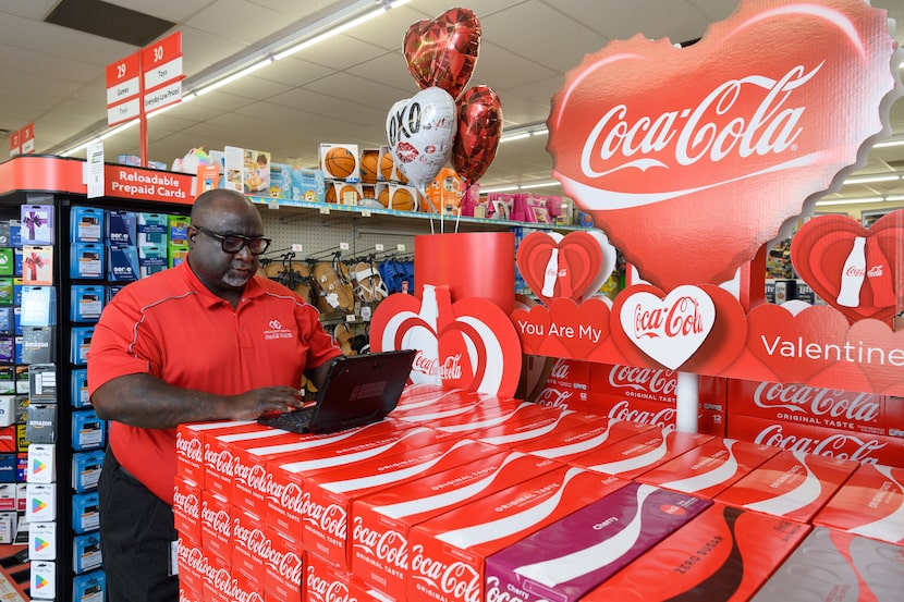 African American man in a Coca-Cola t-shirt works on a laptop resting on a Coca-Cola display...