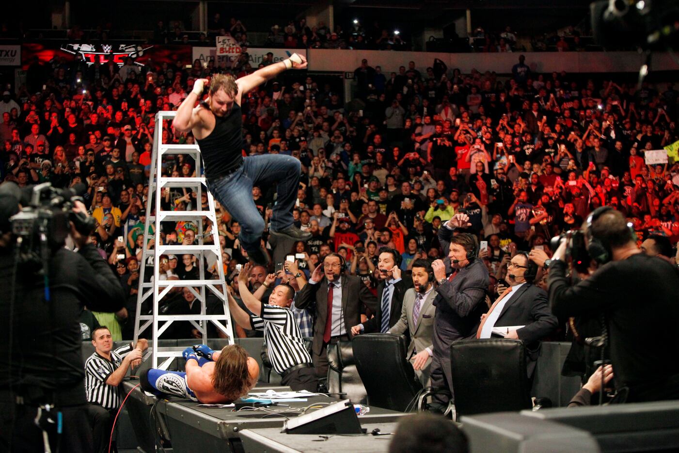 Dean Ambrose, left, leaps off a ladder onto WWE world champion AJ Styles as he lays on a tv...