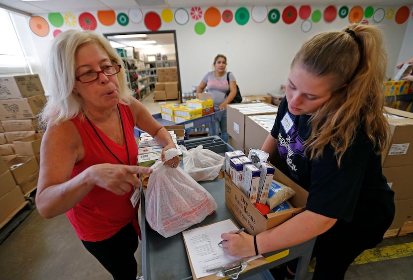 Volunteers Ellen Brude (left) and Grace Dickerson, 15, gather up groceries for client Lorena...