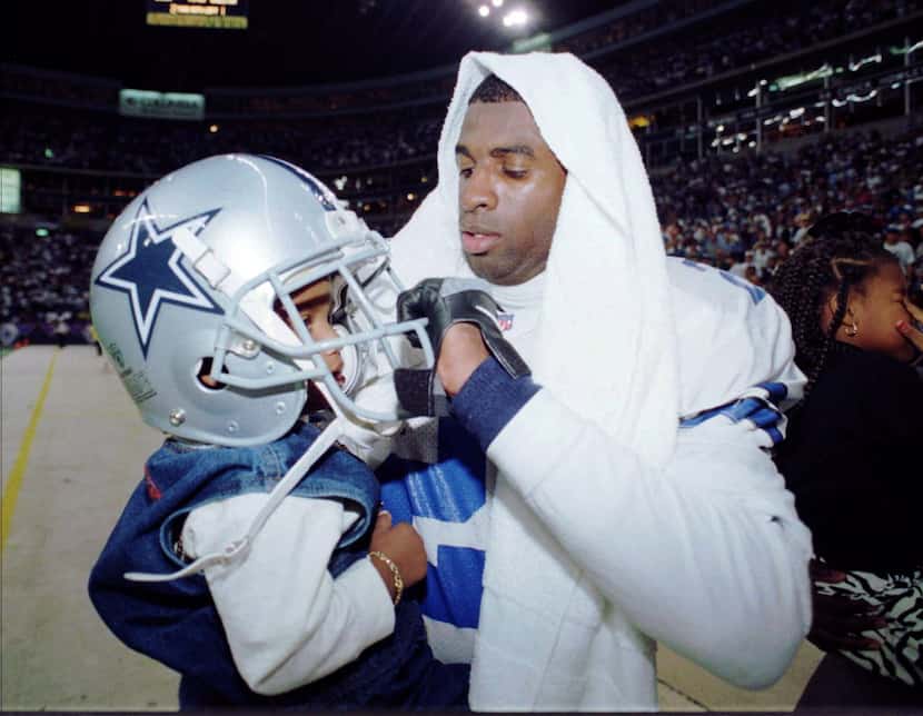 Dallas Cowboys' Deion Sanders, right, places his helmet on his son Deion Sanders, Jr. after...
