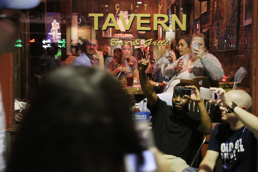 Patrons at the City Tavern react to protesters marching by along Main Street during a...