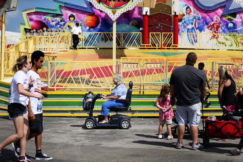 A woman drives her scooter past a ride at the State Fair of Texas at Fair Park in Dallas on...