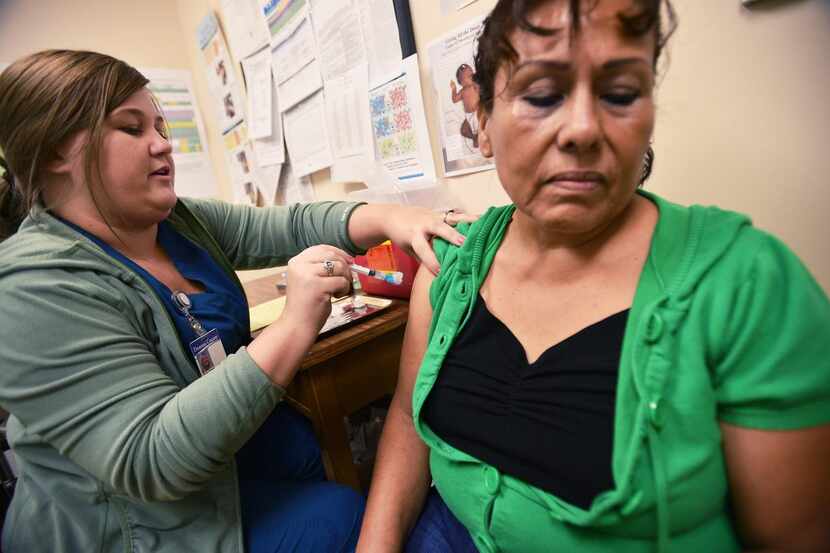 Christina Guerrero  winces a bit as Tara Reed gives her a flu shot at the Denton County...