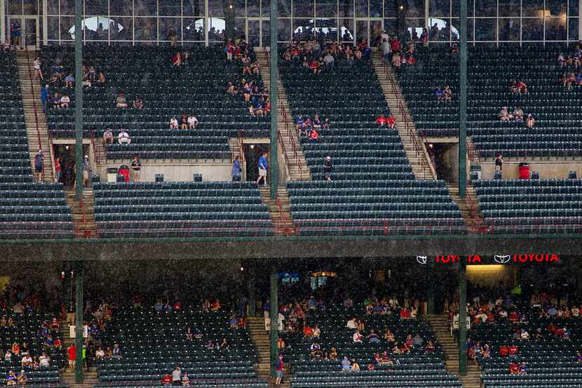 Fans take cover during a rain delay before a baseball game between the Texas Rangers and the...