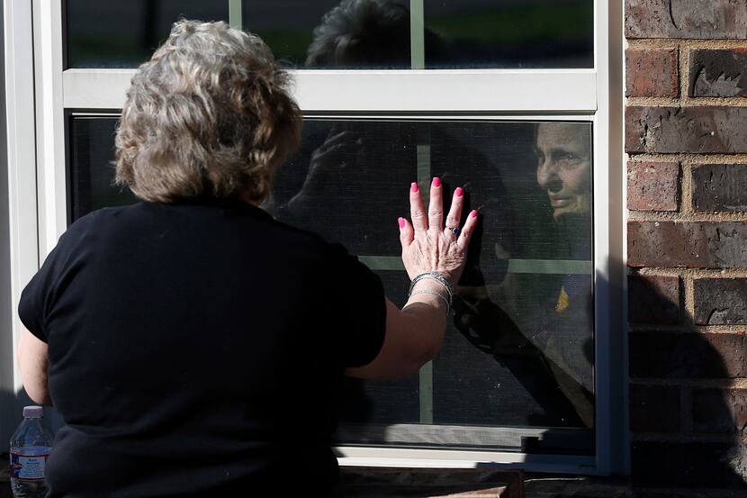 Cindy Goleman waves goodbye to her mother Peggy White from opposites sides of the window at...