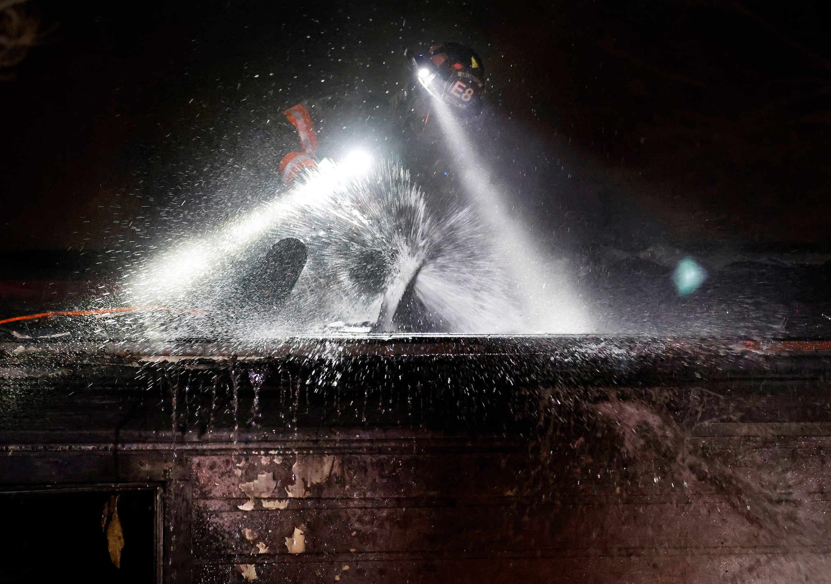 An Arlington firefighter sprays hot spots on the roof as the department battled a two-alarm...