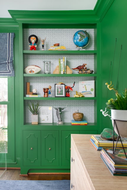 Green bookcase with wallpaper accents and knickknacks on the shelves