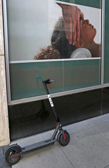 A rental scooter is parked alongside a business poster on Commerce Street in downtown Dallas.
