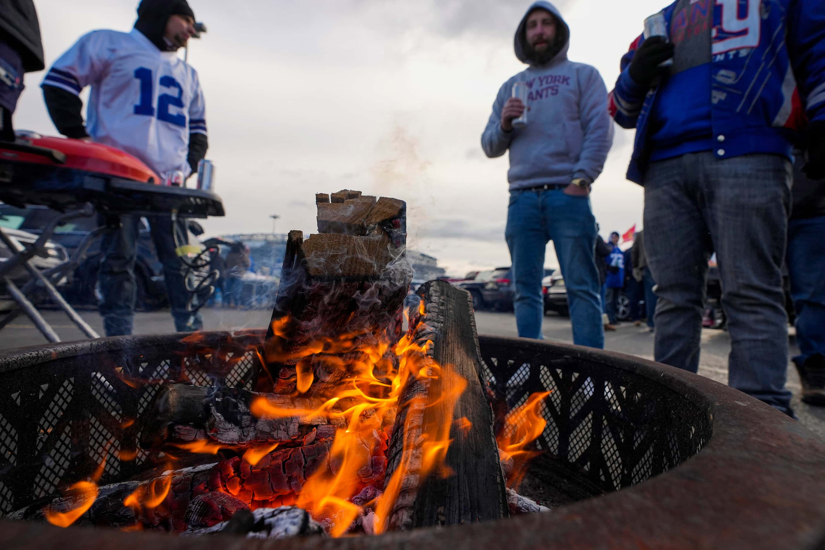 Fans gather around a fire while tailgating before an NFL football game between the New York...