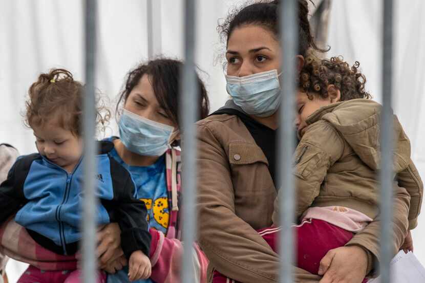 Una mujer carga a un niño pequeño mientras espera con otras familias migrantes antes de se...