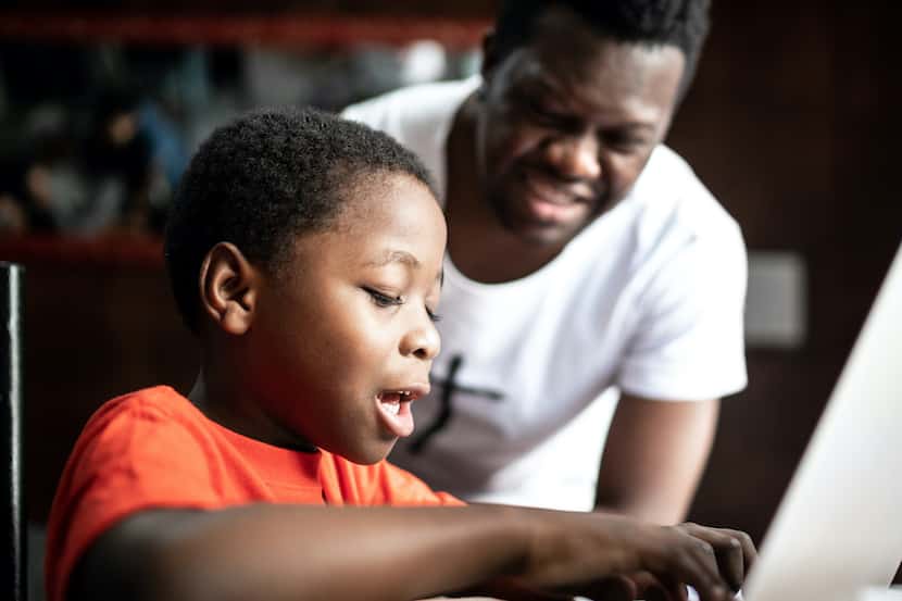 A black tutor helps a black student with his online studies.