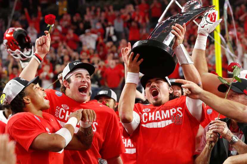 Utah quarterback Cameron Rising, right, holds up the trophy and celebrates with Dalton...