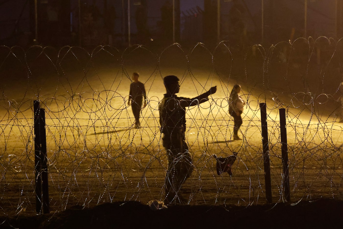 Migrant people wait behind fortified concertina wire on the U.S. side of the Rio Grande...