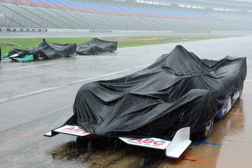 Race cars are covered by tarps during a thunderstorm which stopped an IndyCar auto race at...