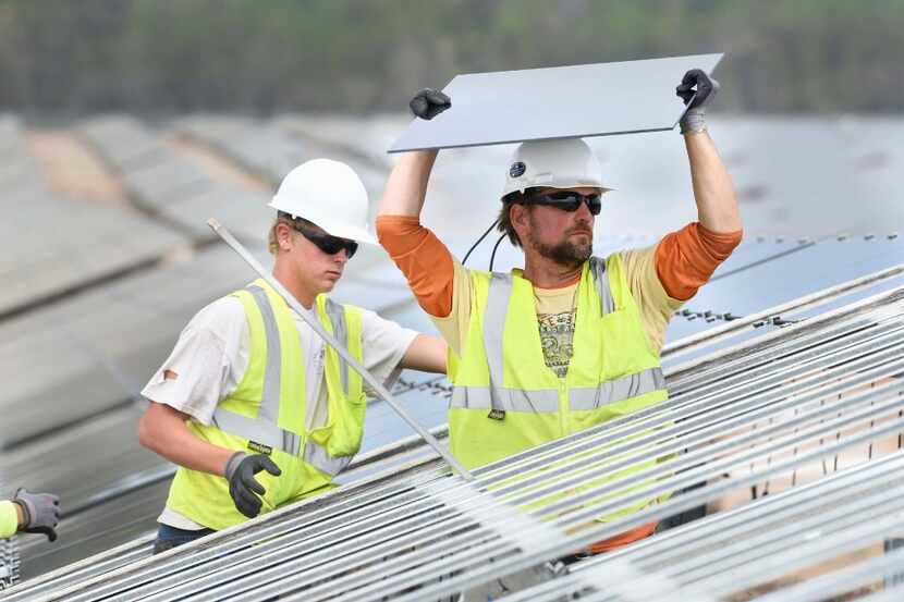 James Drane, right, and Logan Fickett install solar panels on a new solar energy project...