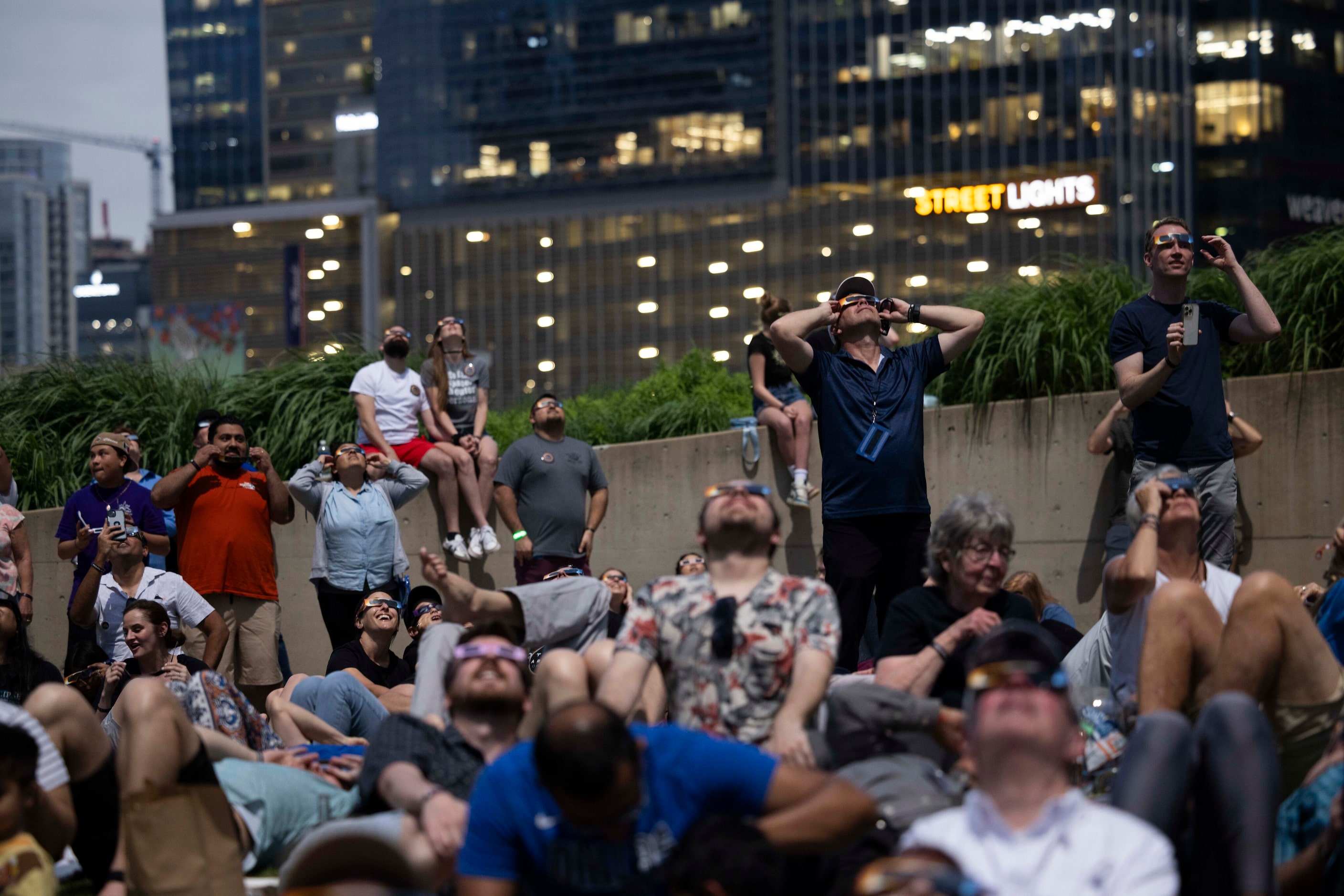 People watch the eclipse enter totality as building lights turn on behind them during the...