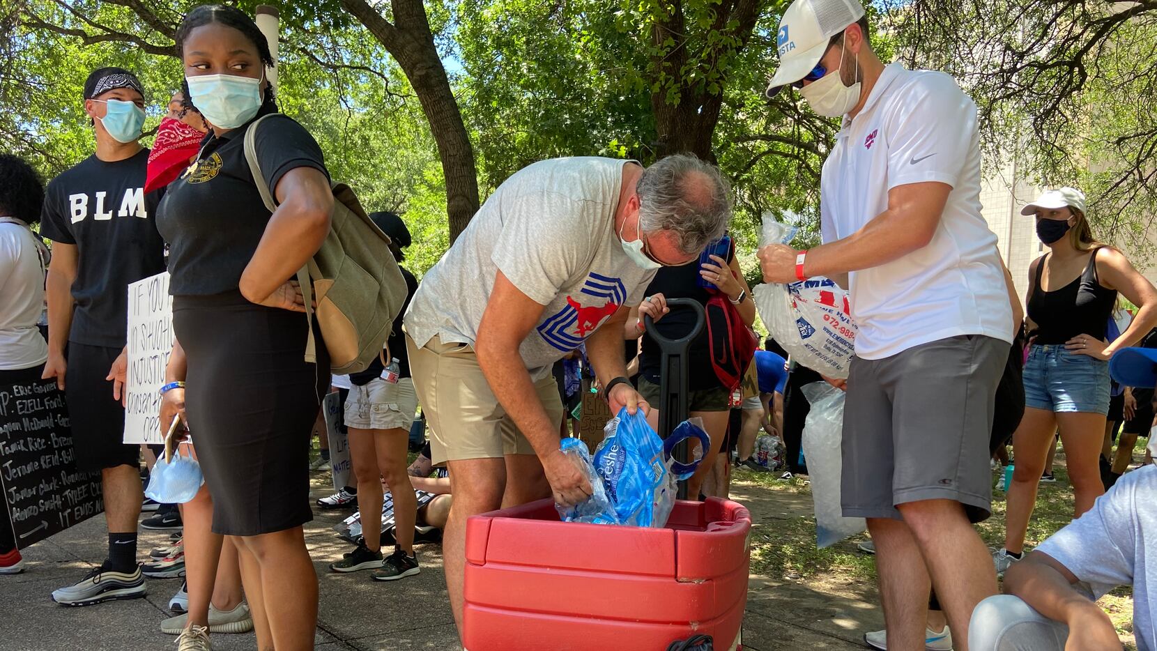 SMU football coach Sonny Dykes passes out water bottles while attending a protest at Dallas...