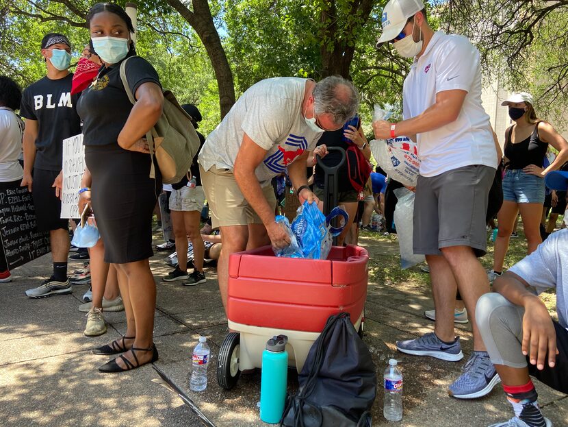 SMU football coach Sonny Dykes passes out water bottles while attending a protest at Dallas...