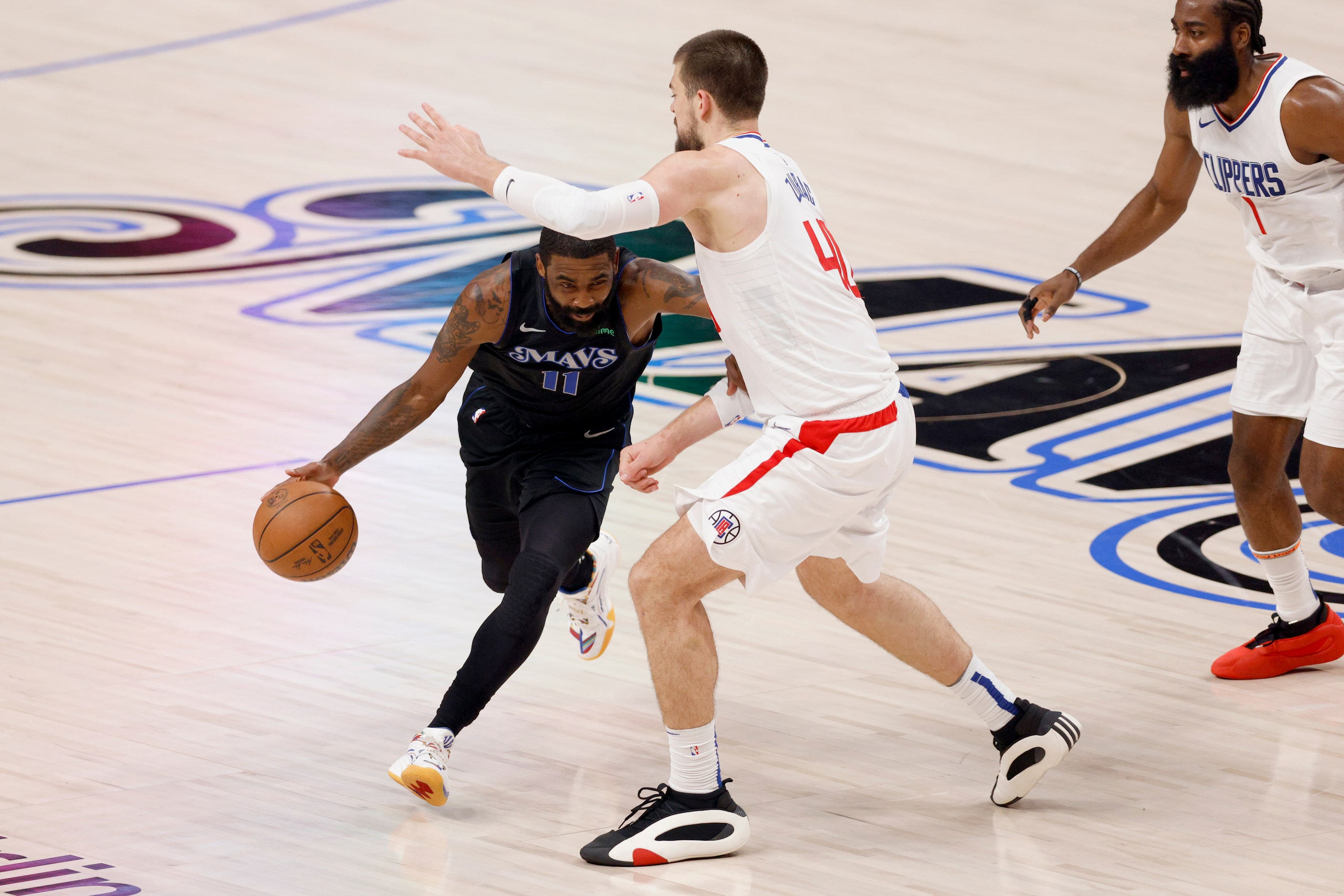 Dallas Mavericks guard Kyrie Irving (11) dribbles under the arm of LA Clippers center Ivica...