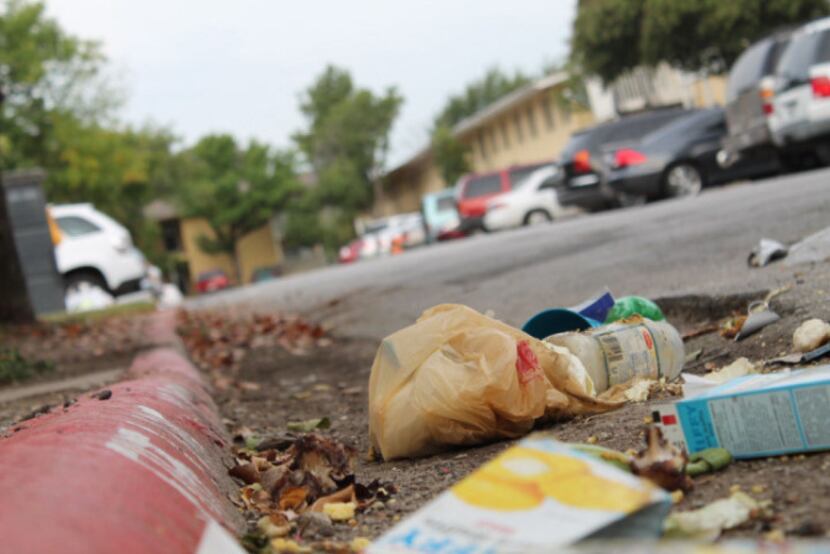 Trash litters a parking lot pothole in Oak Villas Apartments where Irving code violations...