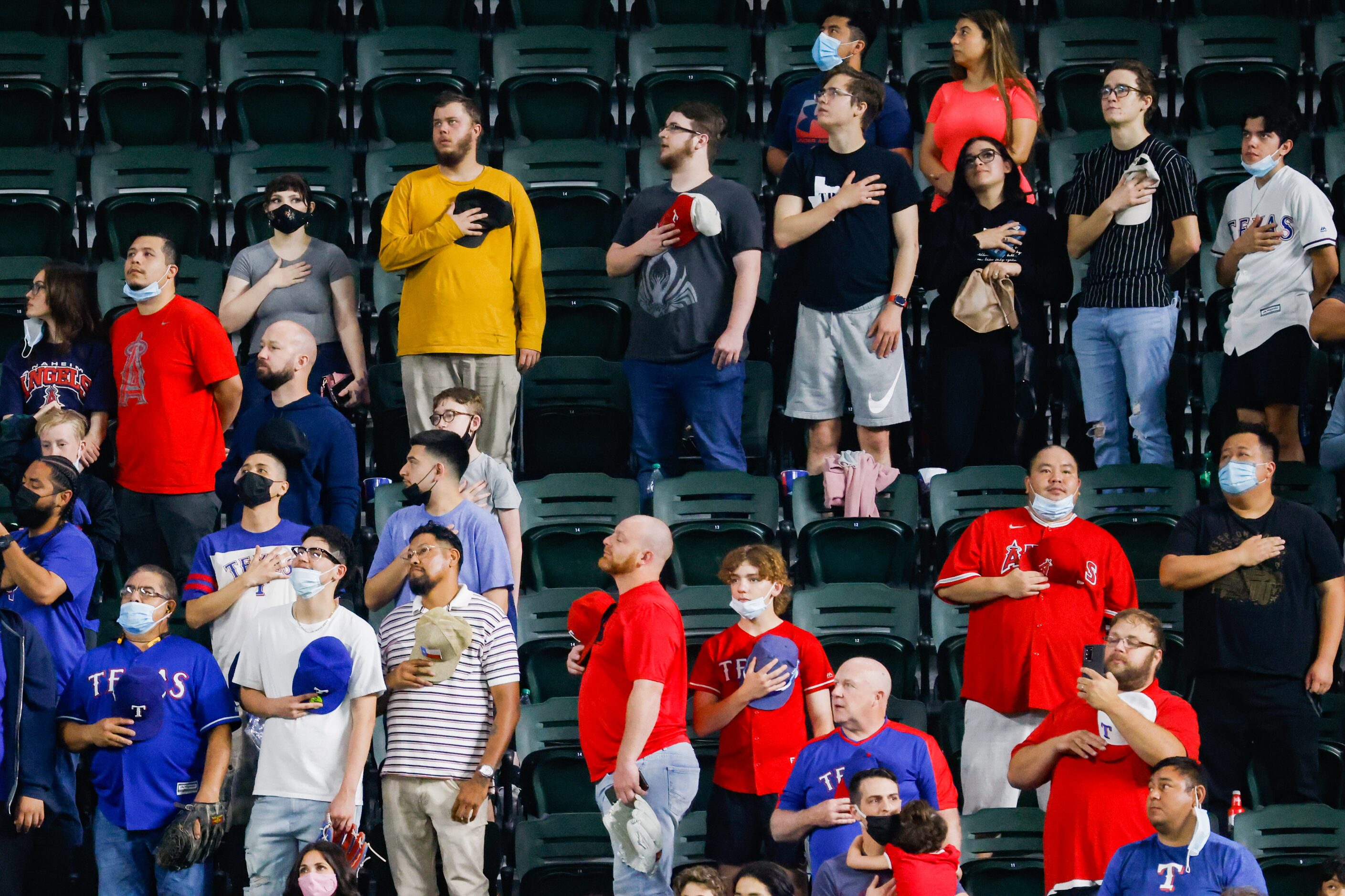 Fans some with masks and some without stand for the pledge before the first inning of a MLB...