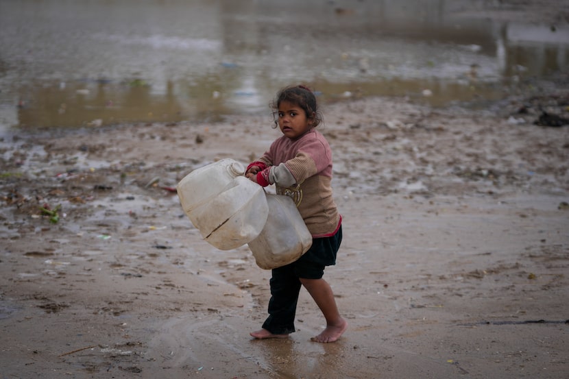 A young girl walks barefoot, carrying empty jerrycans to collect water, after overnight...