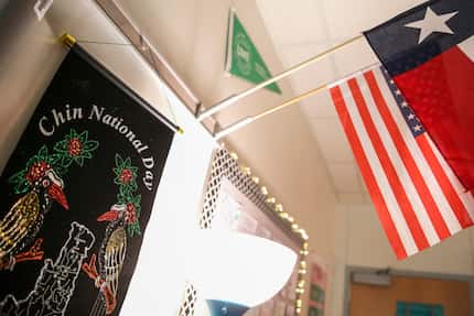 A Chin National Day banner hangs below the United States and Texas flags in a classroom...