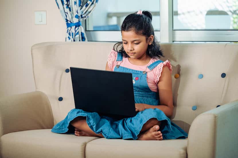 Young girl sits on couch working on a laptop.