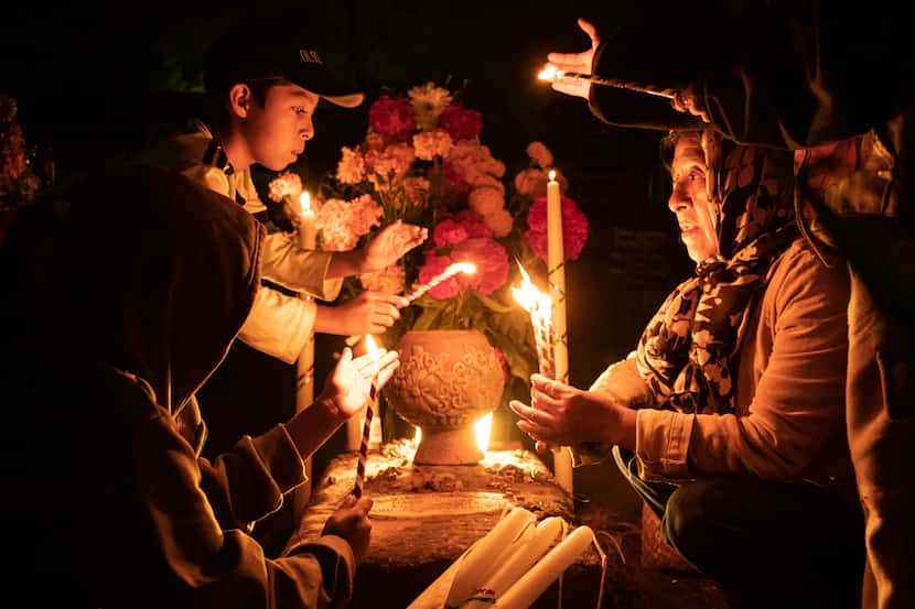 La gente sostiene velas sobre una tumba decorada con flores en un cementerio en Atzompa,...