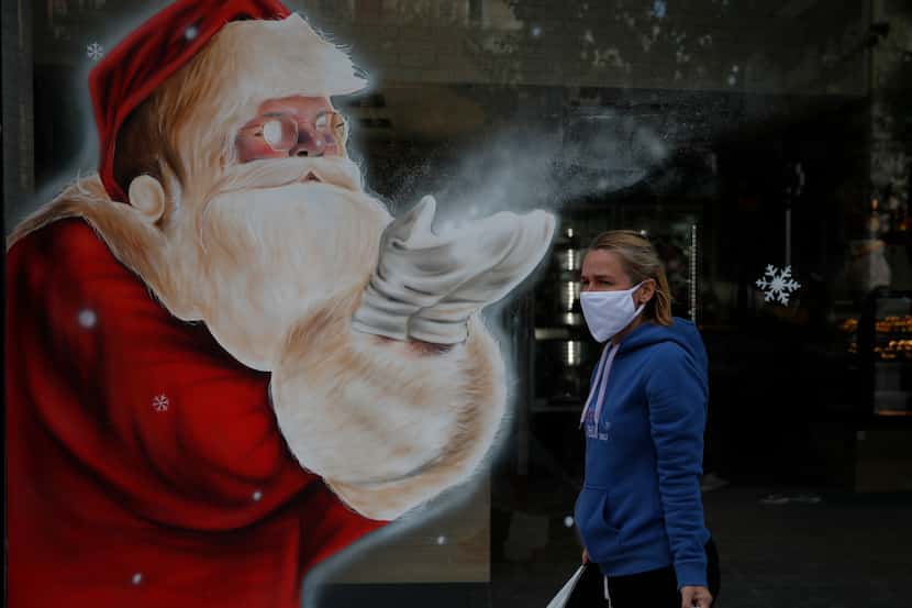 A woman wearing a face mask passes a Santa Claus mural that decorates the store window of a...