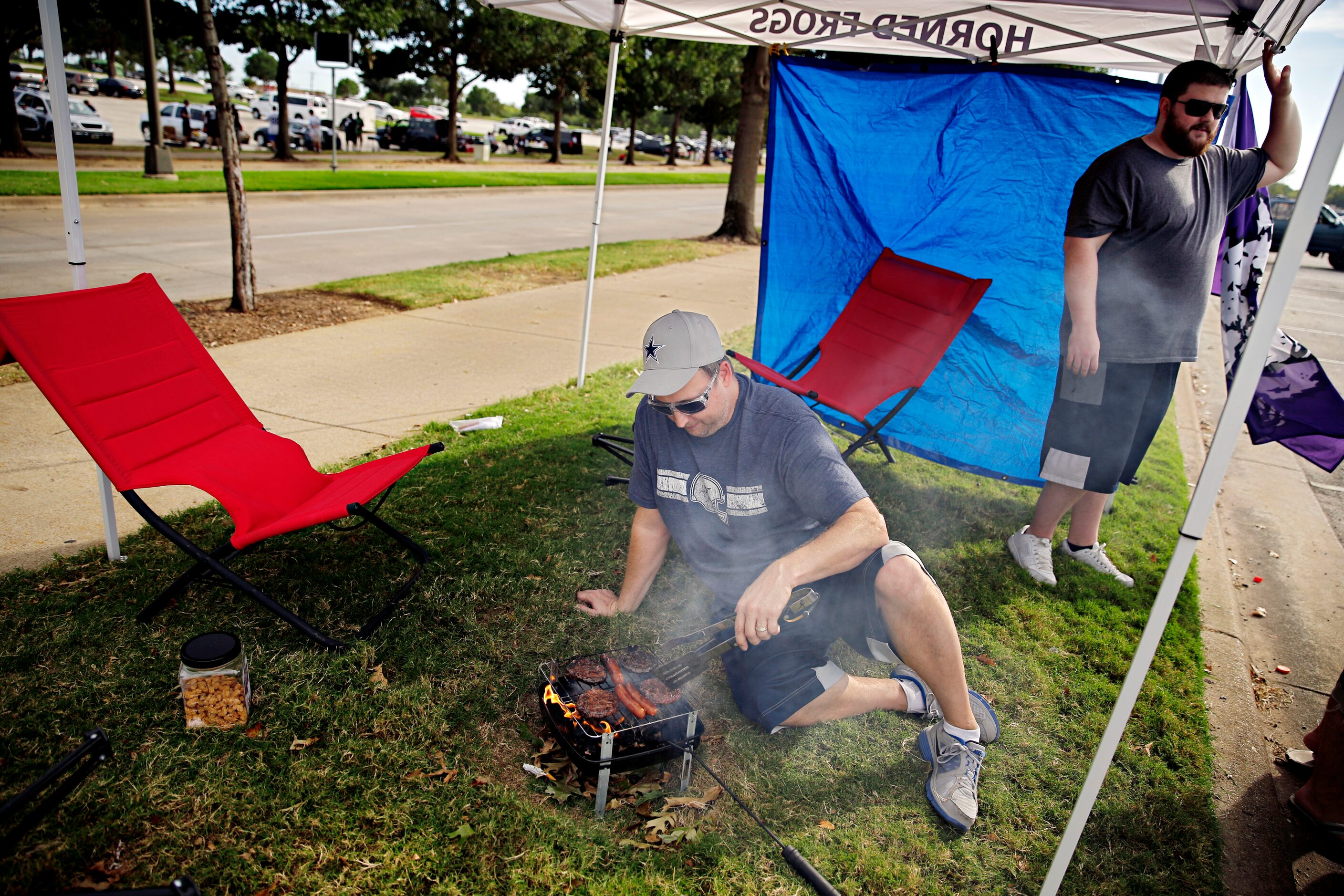 Mark Cobb (center) mans a grill as Clint Coleman looks on before the Dallas Cowboys game...