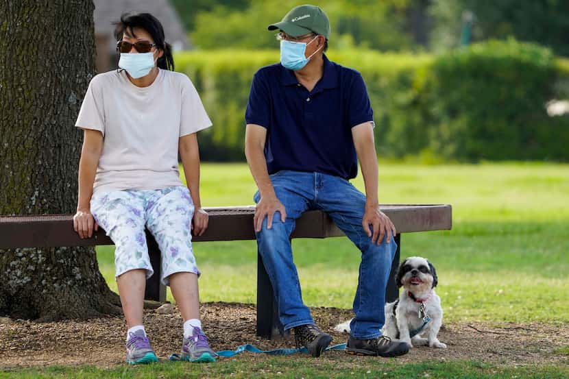 Jeff and Raynette Ho wear face masks as they sit with their dog at Custer Park on Thursday,...