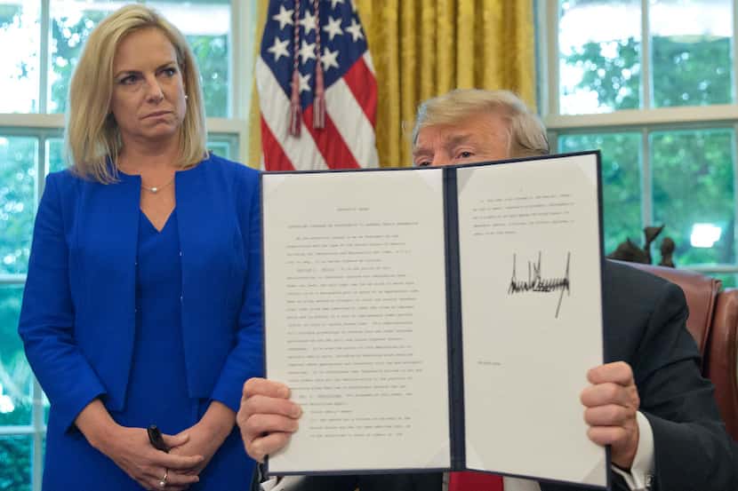 President Donald Trump holds up an executive order he signed on Wednesday. Looking on is...