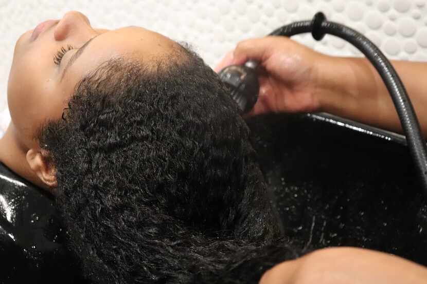 A woman has her hair washed by a Pressed Roots stylist.