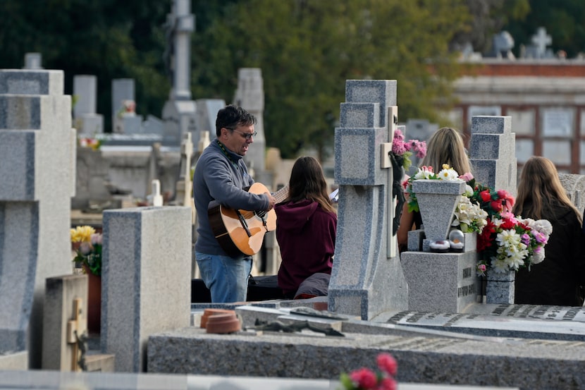 A man sings and plays a guitar as others gather around a grave in the Almudena cemetery...