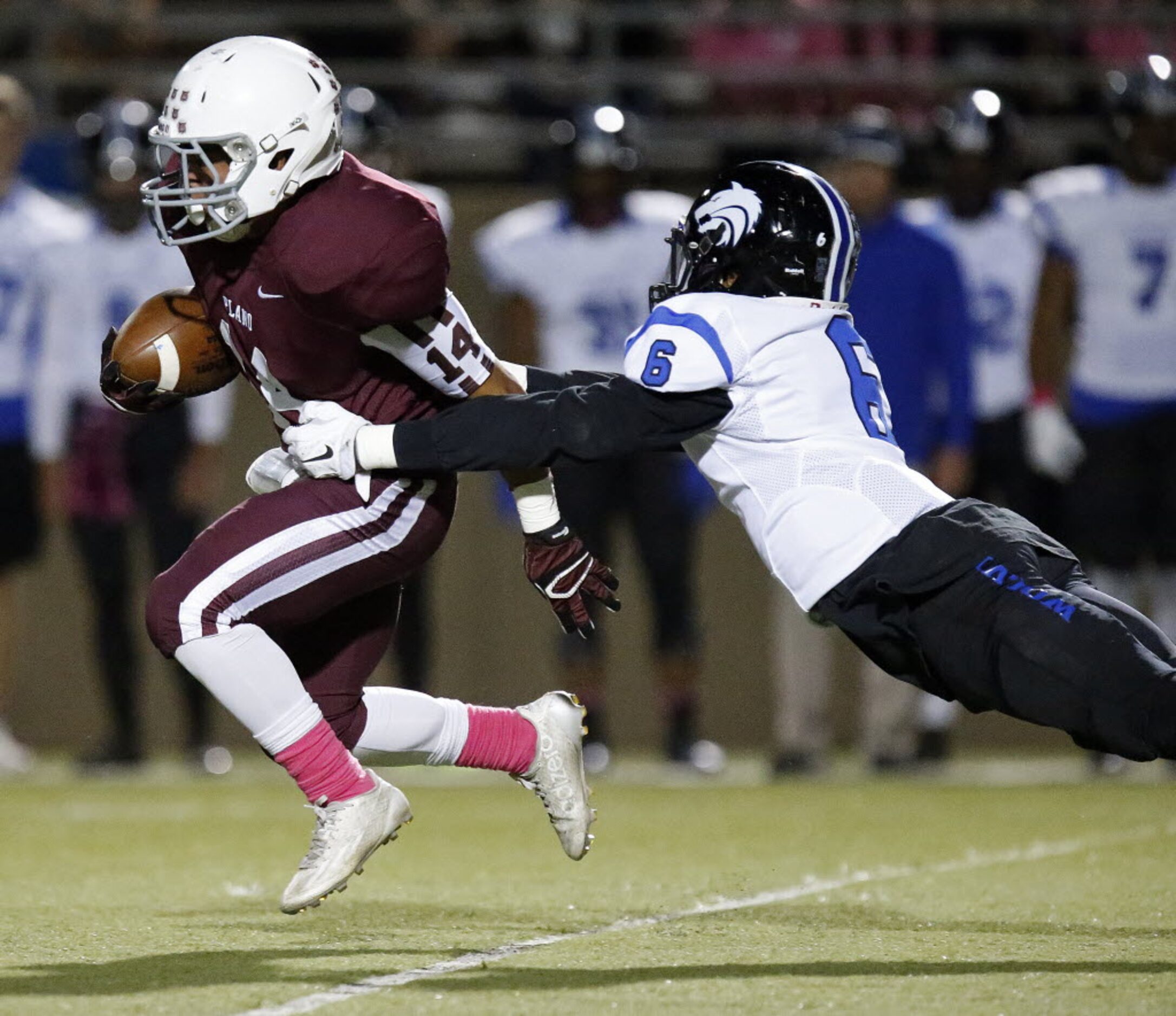 Plano High School kick returner Lopaka Yoro (14) is in the grasp of Plano West defender...