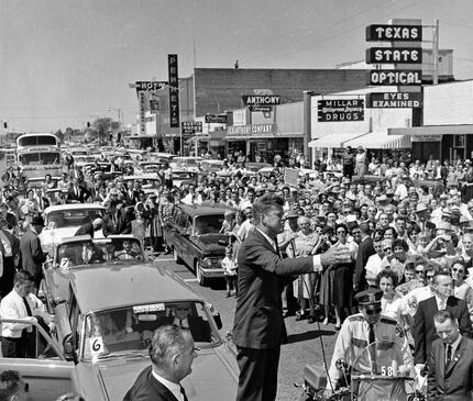 John F. Kennedy stands on the trunk of a car to deliver a speech in front of Millar Drugs in...