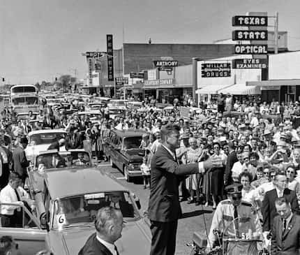 John F. Kennedy stands on the trunk of a car to deliver a speech in front of Millar Drugs in...