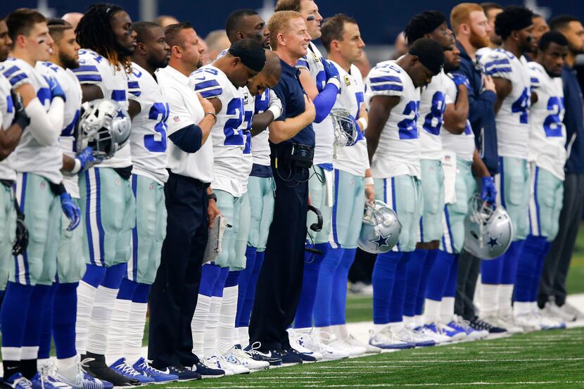 Dallas Cowboys players and coaches stand along the sideline for the national anthem before...
