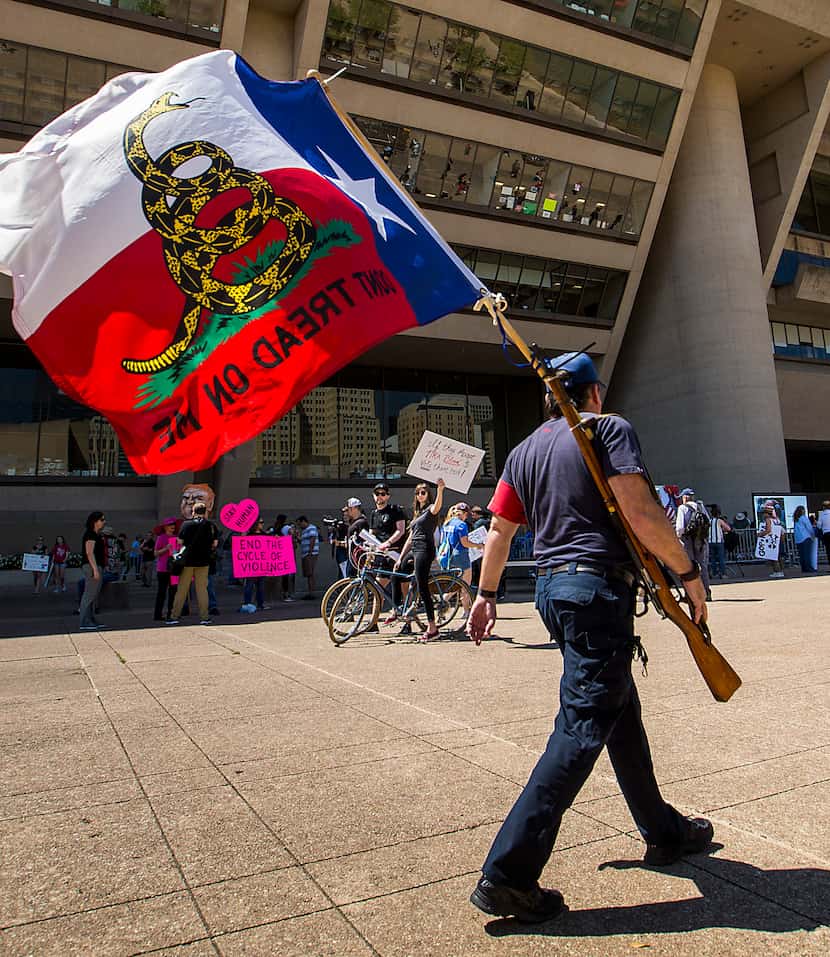 Gun rights advocate Brad McClain carries a rifle and flag as he walks past a rally of gun...