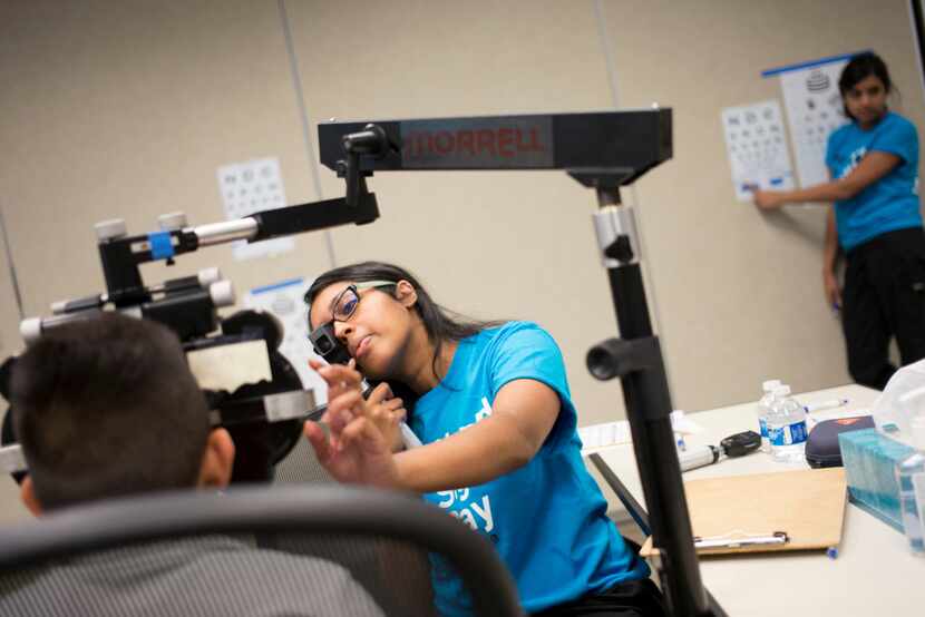 Volunteer Ashley Varghese (center) exams a Carrollton ISD student's eye during the free eye...