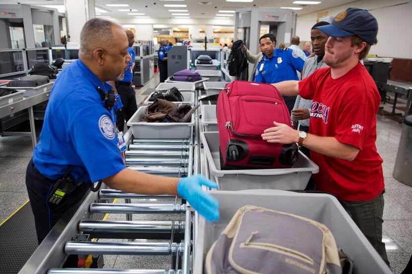 A TSA official helps passengers load their carry-on belongings onto an automated conveyer...
