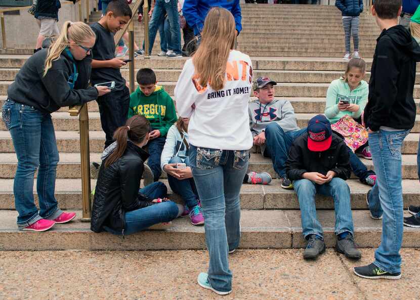 Teens check their smartphones outside the Natural History Museum in Washington on April 8,...