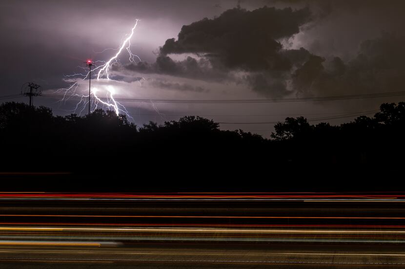Lightning bolts fill the sky as car lights streak by on Highway 360 during an evening storm...