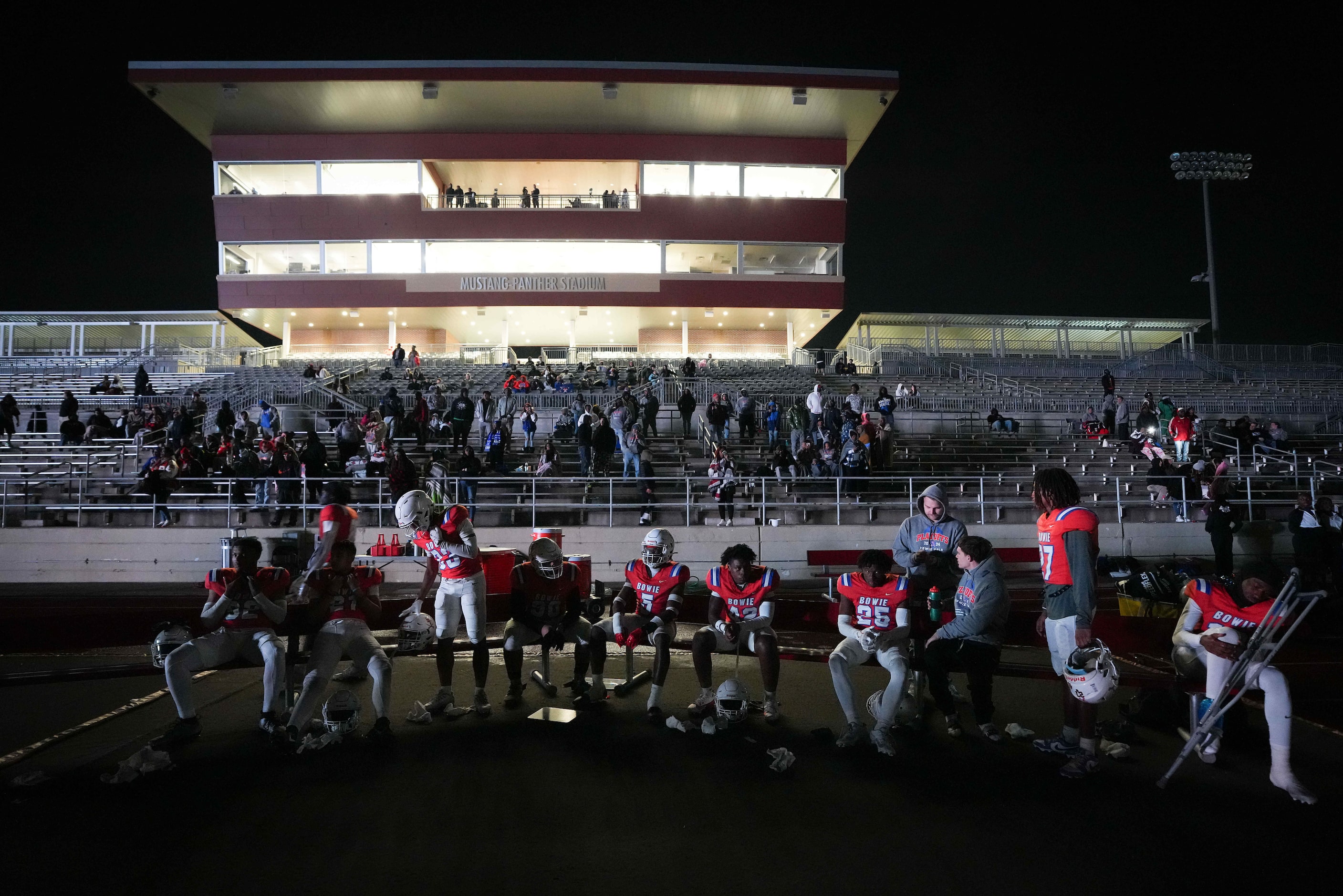 Arlington Bowie players wait on a darkened sideline during a delay due to the main stadium...