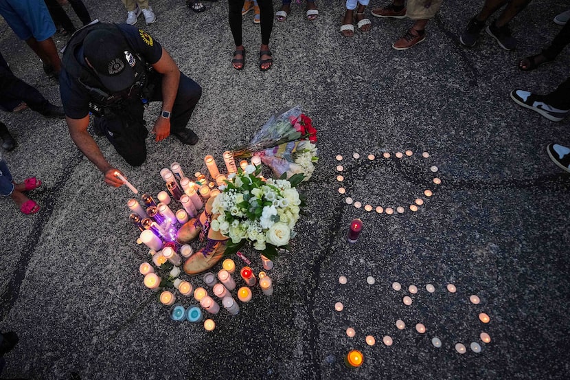 A Dallas police officer places a candle on a memorial surrounding the fraternity boots of...