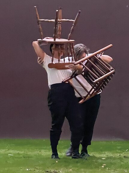 Two women dressed in black and white holding chairs.